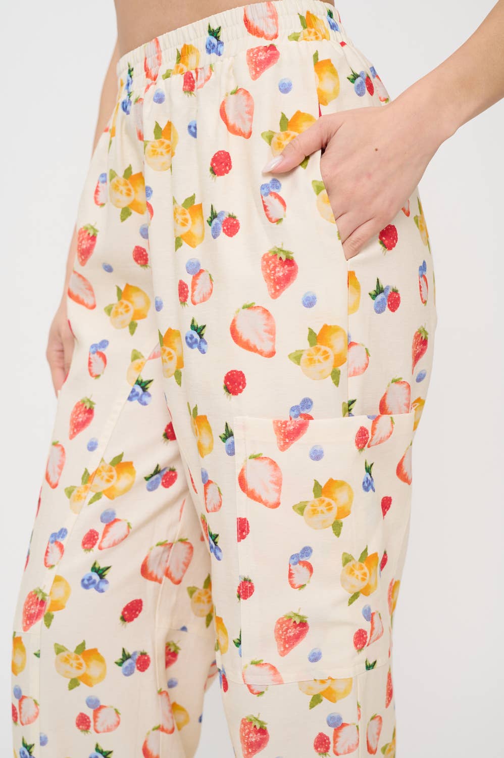 Close-up side view of berry print cargo pants with a relaxed fit, elastic waistband, and a functional side pocket, featuring a vibrant fruit pattern.